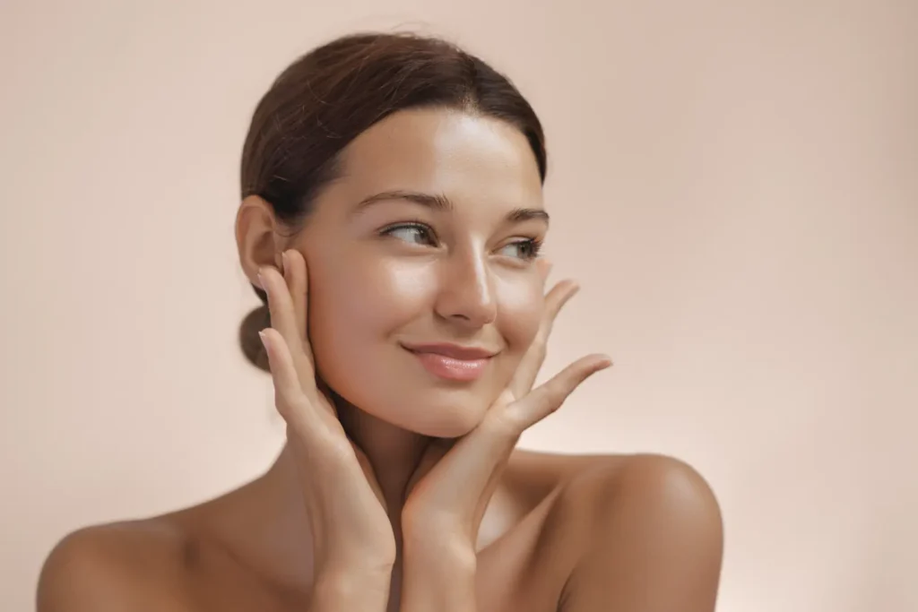 Woman touching her face with both hands against a beige background