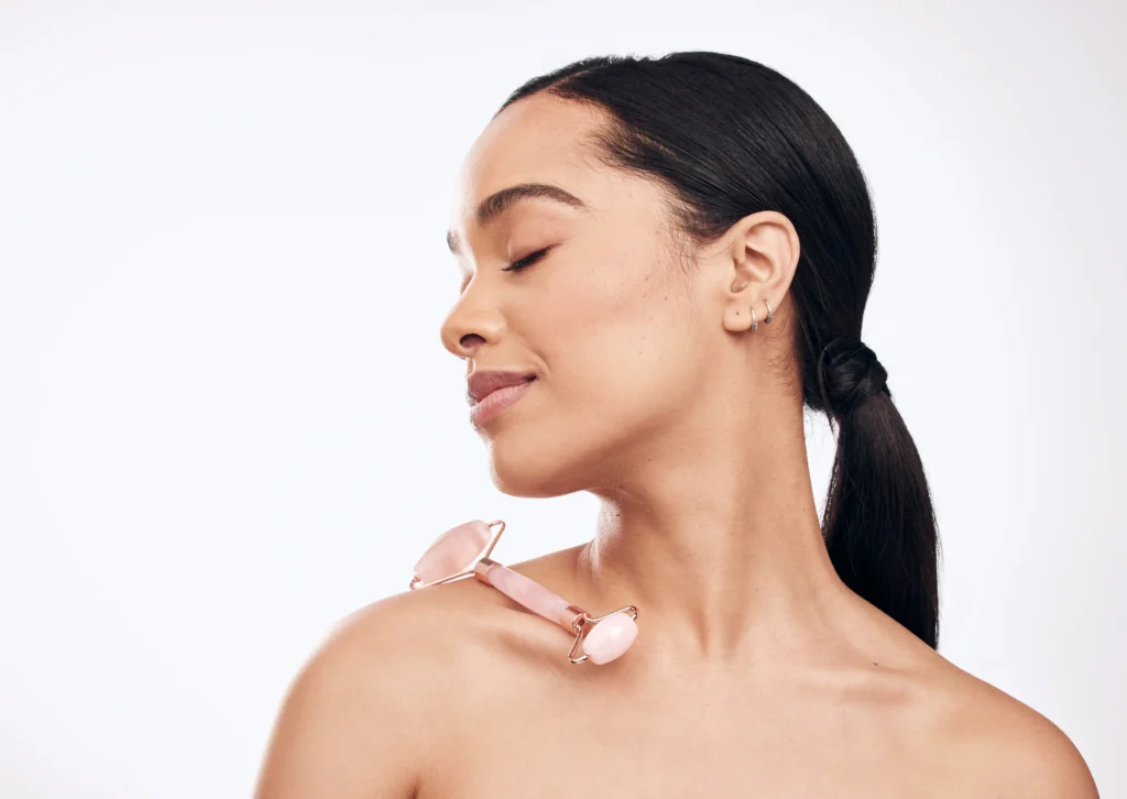 Woman holding a facial roller on her shoulder with eyes closed against a light background