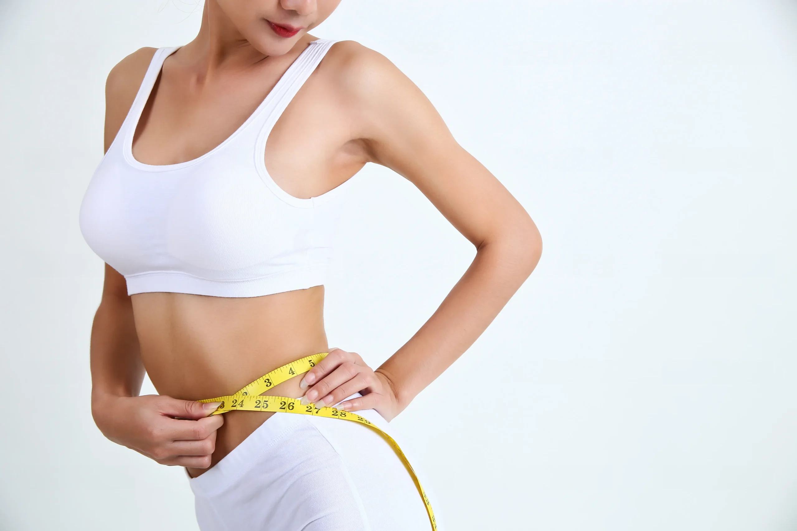Woman in white activewear measuring her waist with a yellow tape measure