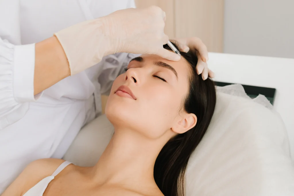 Practitioner marks the forehead before an injectable facial treatment while the patient rests with eyes closed.