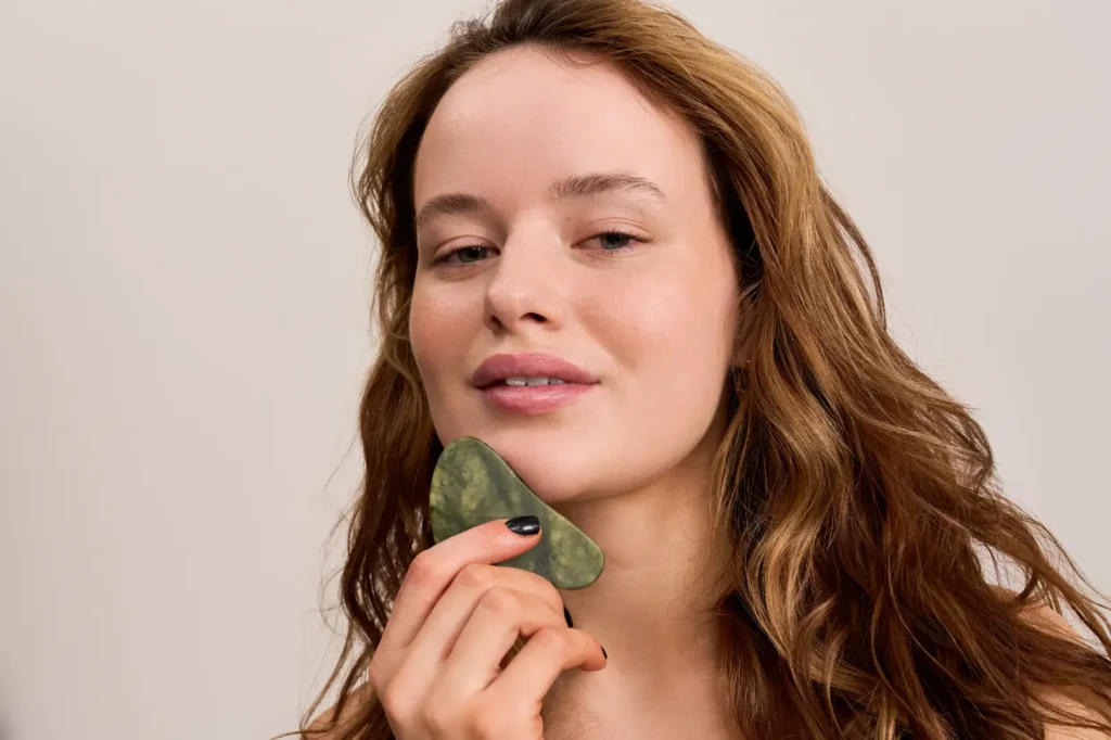 Woman holding a green facial massage tool against the underside of her chin.