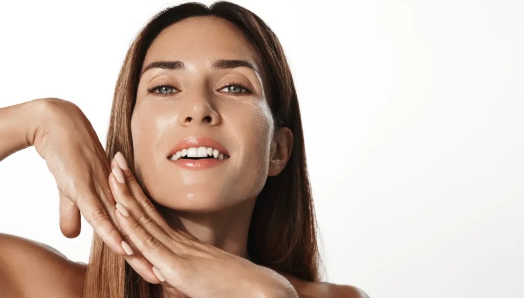 Front-facing woman with straight brown hair holding both hands beside her jawline.