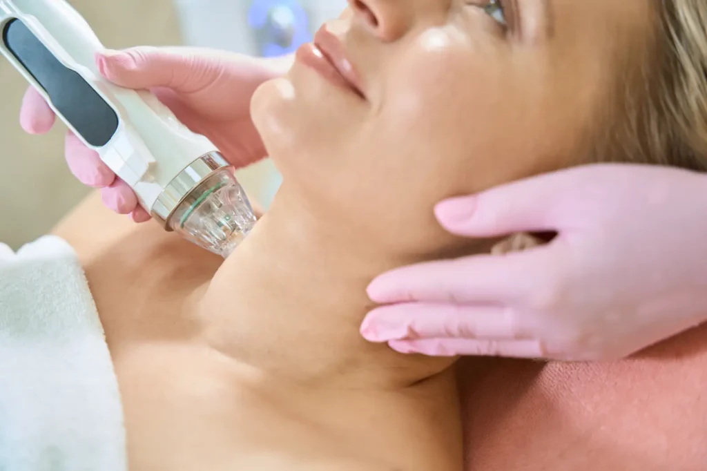 Gloved practitioner holding a treatment handpiece against the side of a woman's neck.